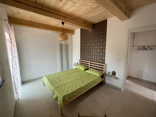 Helles Schlafzimmer mit Doppelbett, grüner Bettwäsche und Holzdecke.