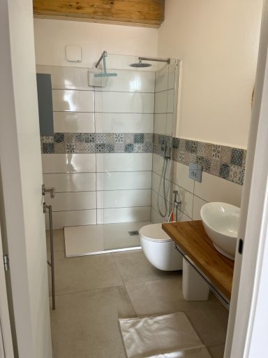 Modernes Badezimmer mit Dusche, Waschbecken und WC, helle Fliesen und Holzdetails.