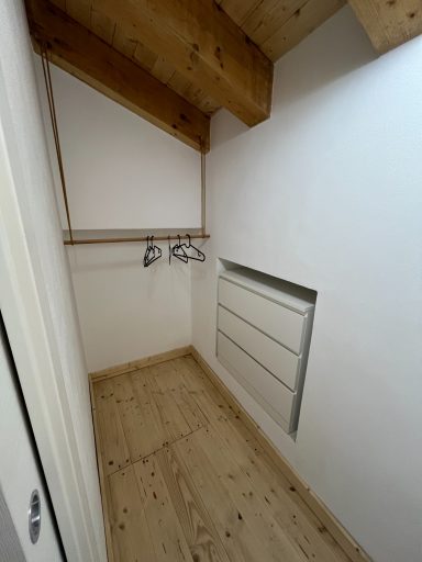 Kleiner Raum mit Holzregalen, Kleiderbügeln und einem Heizkörper an der Wand.