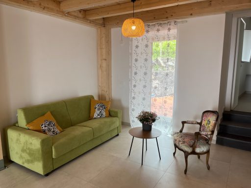 Ein gemütliches Wohnzimmer mit grünem Sofa, Beistelltisch und einem kleinen Stuhl.