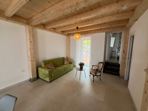 Helles Wohnzimmer mit grüner Couch, Holzdecken und Fenster zur Terrasse.