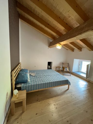 Helles Schlafzimmer mit Holzdeckenbalken, Bett und kleiner Nachttisch.