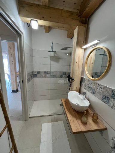 Helles Badezimmer mit Dusche, runder Spiegelschrank und Holzregal.