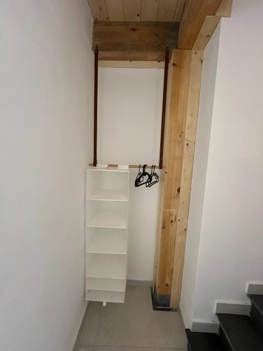 Schmale Nische mit einem weißen Regal und einem Holzständer, an einer Wand.