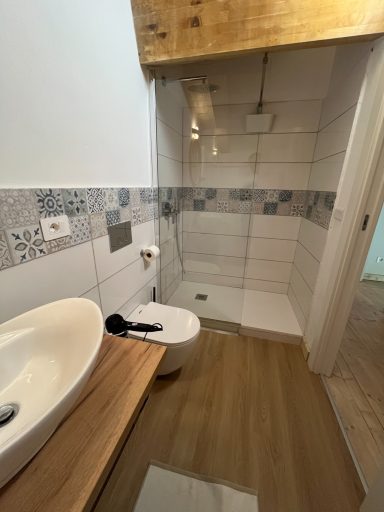 Badezimmer mit Dusche, Waschbecken und Toilette auf Holzfußboden.
