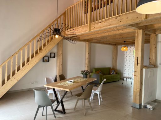 Wohnzimmer mit Holzbalken, Essbereich und grüner Couch unter einer Treppe.